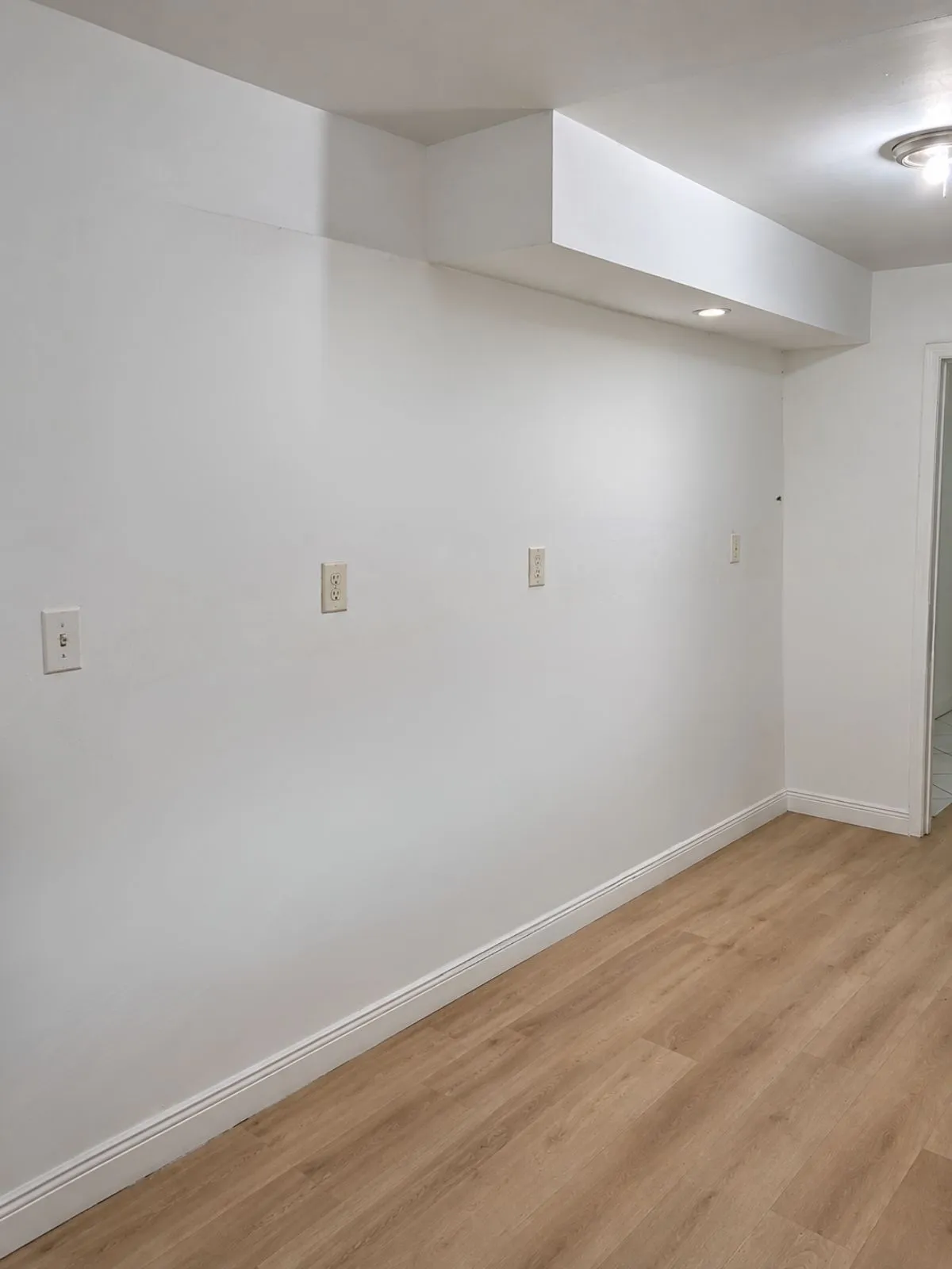 Empty room with plain white walls and wood-look flooring